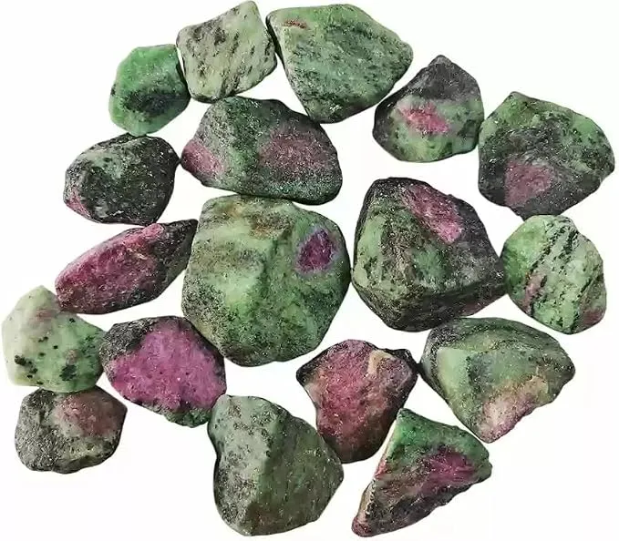 A scattered pile of numerous small, raw ruby zoisite crystal chunks isolated on a white surface, displaying the characteristic mottled pattern of green zoisite and deep red ruby inclusions