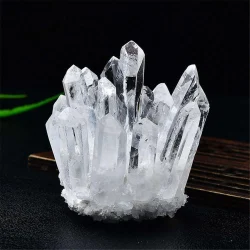 A clear quartz crystal cluster resting on a dark, slatted wooden surface, set against a solid black background.