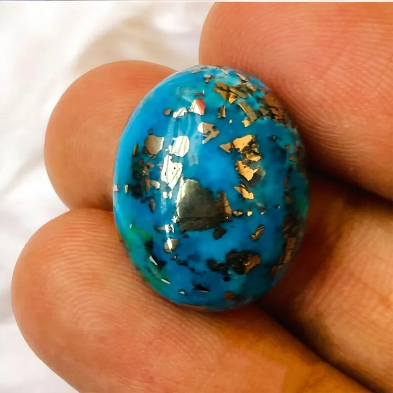 Side-angle studio shot of a lab certified, double-polished natural Irani Firoza oval cabochon on a pure white background, highlighting dense metallic brassy-gold pyrite inclusions across a sky-blue Persian turquoise body for bracelets and talismans