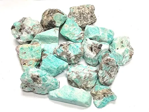 close-up of a hand holding a large, raw Amazonite crystal chunk indoors near a window, highlighting its textured surface and vivid aqua-green color.
