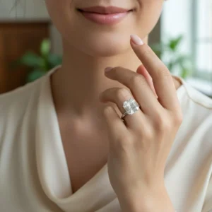 A smiling woman wearing an elegant cream blouse showcasing a large, brilliant Asscher cut moissanite solitaire engagement ring on her hand.