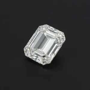 Slightly angled close-up of a loose Emerald cut moissanite resting on a dark grey background, highlighting the depth, strong lines, and brilliant light reflection of its step-cut facets