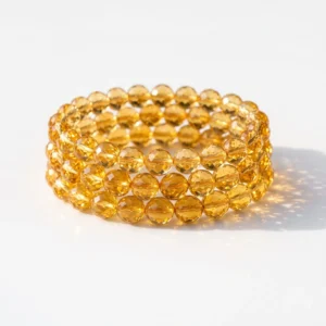 Stack of three AAA grade natural citrine 8mm diamond cut crystal bracelets sparkling on a clean white background.