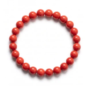 Top-down commercial product photograph of a natural, premium gem-grade Red Coral 8mm beaded bracelet made of approximately twenty-four (24) small, perfectly round beads on a pure #FFFFFF white background. The beautiful, opaque beads showcase a rich, natural, deep scarlet-to-oxblood red color with subtle, organic variations in hue. Some beads may display very faint, natural graining or tiny, barely perceptible white or darker natural pinpoint markings characteristic of genuine, un-dyed marine coral. Highly polished to a smooth, glassy, and slightly waxy luster that catches the soft, diffused studio lighting. Strung tightly in a neat, natural circle on a strong clear elastic cord, the 8mm beads show a uniform, circular shape. Subtle, soft natural drop shadows are cast on the white surface beneath the bracelet, adding depth and grounding. This image is taken from directly above (top-down perspective), with sharp focus and high clarity across all beads, showcasing their natural, vivid red color and polished texture with no camera distortion, props, or background clutter. This natural beauty is ideal for Root Chakra grounding, vitality, and protection.