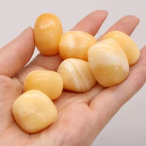 Seven natural honey-yellow calcite tumbled stones with creamy white banding held in an open palm against a clean white studio background for Solar Plexus Chakra healing.