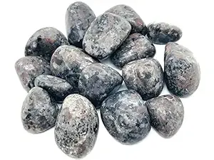 High-resolution flat-lay of fifteen natural Yooperlite tumbled stones arranged on warm natural wood grain, showing smooth tumble polish and distinct charcoal, silver-grey, and reddish-brown syenite inclusions.