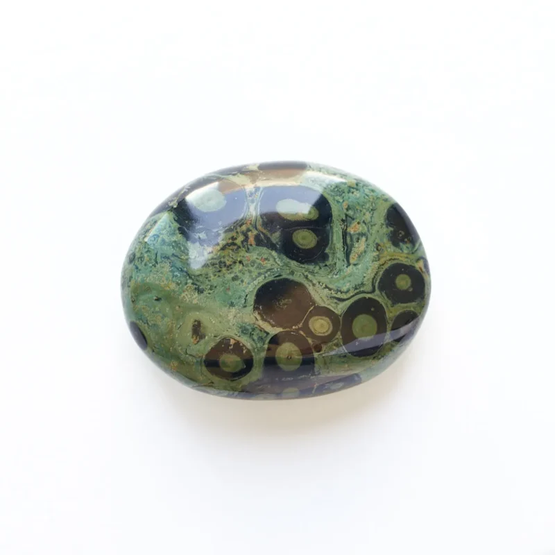 Macro top-down view of a single smooth, oval natural Kambaba Jasper tumbled stone centered on a seamless white background, highlighting sage-green mineral swirls and dark concentric eye orbs for emotional peace and stability.